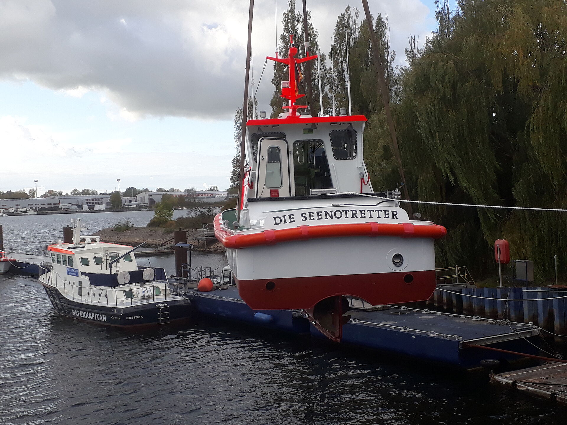 Das Seenotrettungsboot hängt an einem Hafenkran über dem Hafenbecken der Werft. Rückansicht.