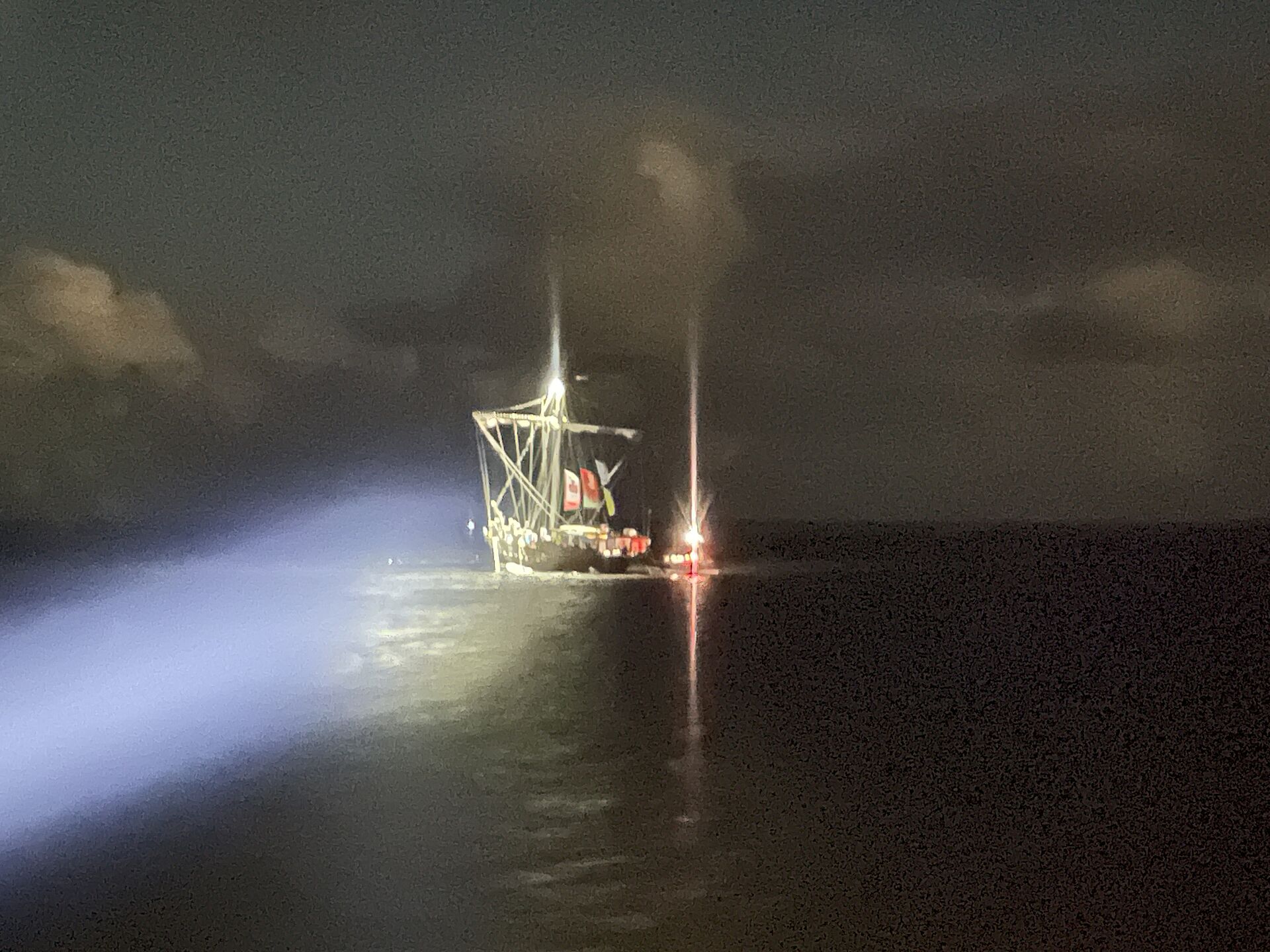 Von einem Suchscheinwerfer wird ein festgekommener Hansekoggen-Nachbau und ein Seenotrettungsboot der DGzRS angestrahlt