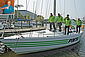 Fünf Vereinsmitglieder der „Pinta-Segelgemeinschaft “an Bord der Yacht, welche in einem Hafen liegt. Oben links in der Ecke ein Foto des Hochseeseglers, von dem die Yacht stammt.