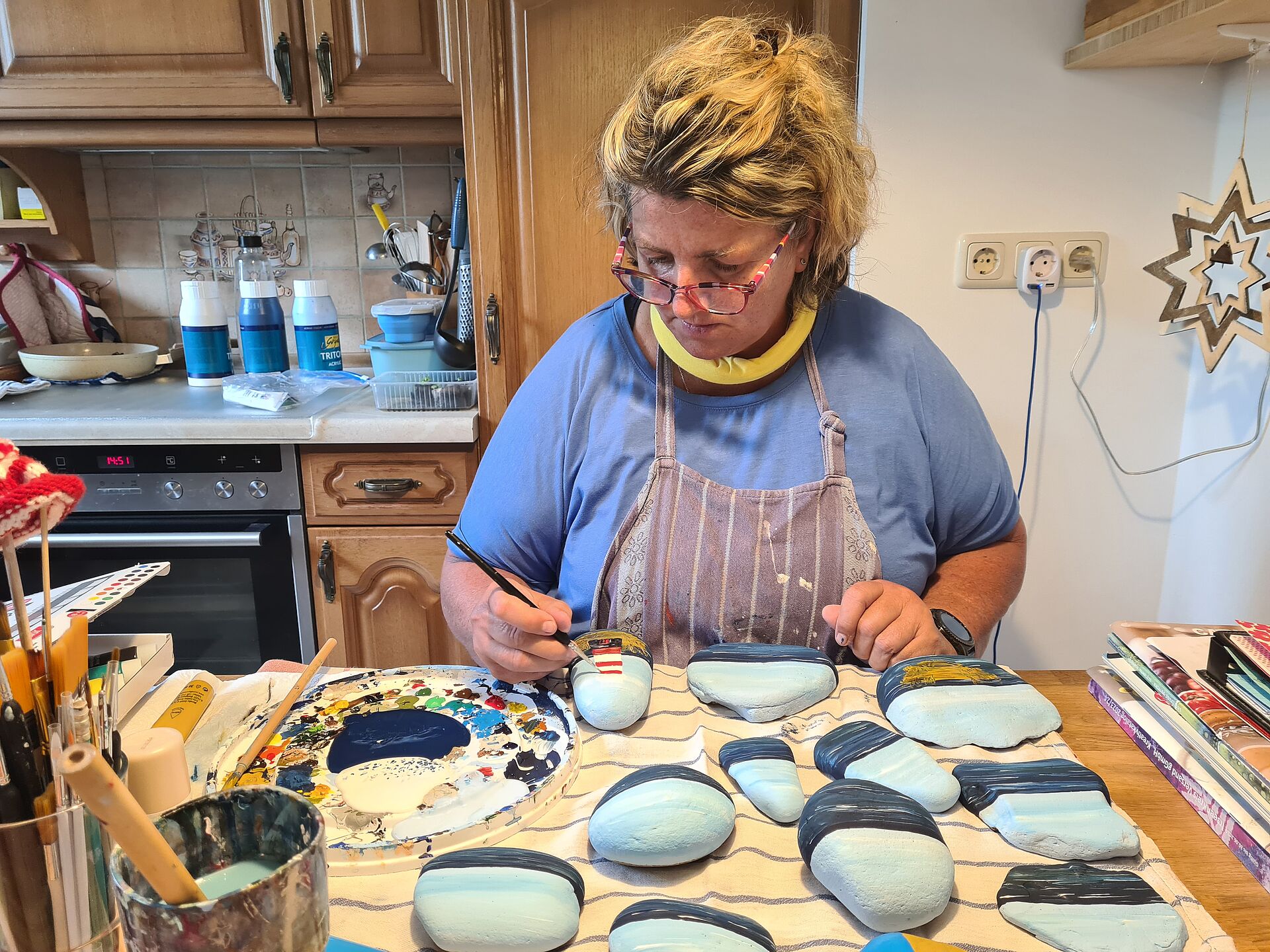 In ihrer Küche bemalt Bettina Lohff die vor ihr ausgebreiteten grauen Steine in farbenfrohe Kunst.