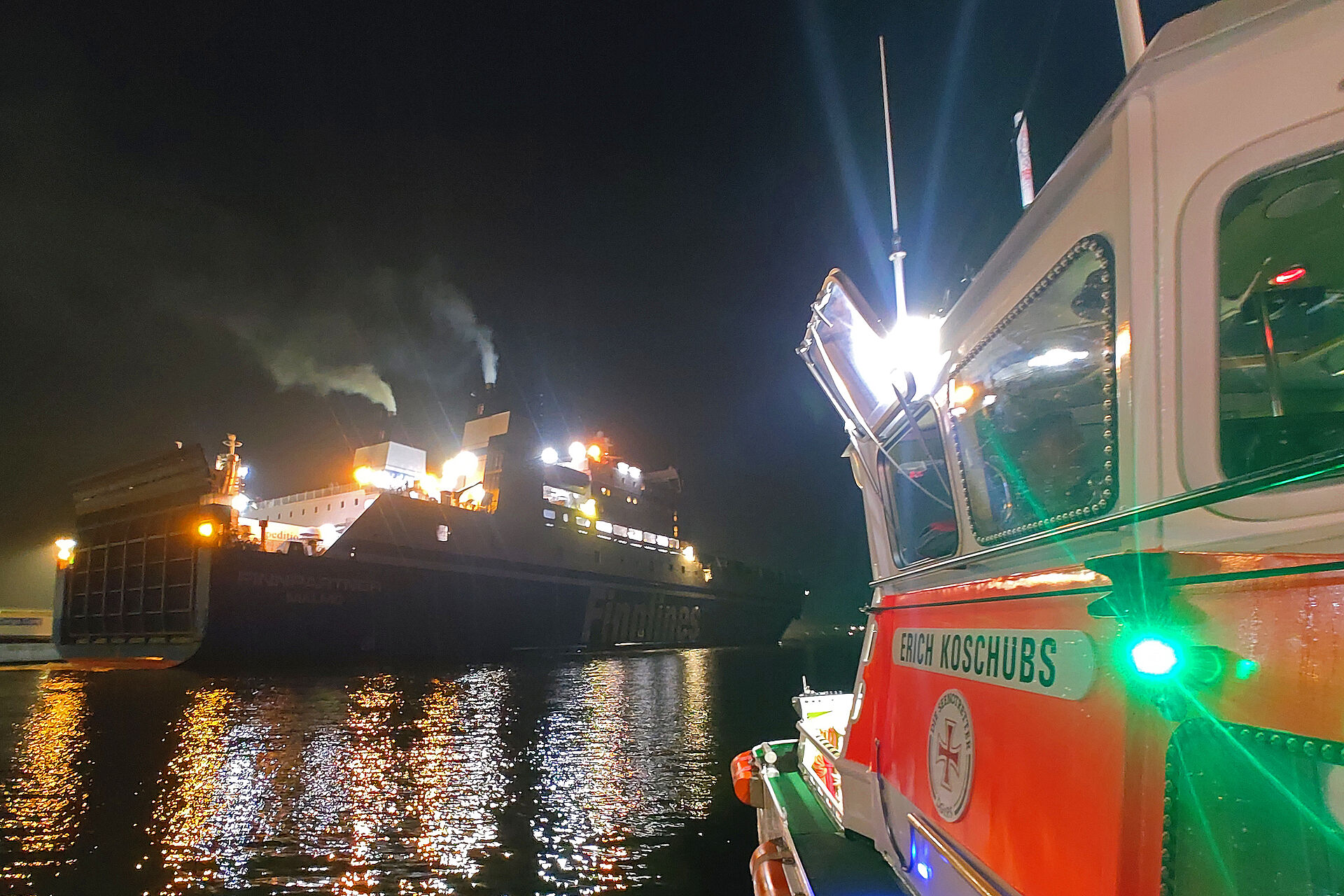 Ein rot-weißes Seenotrettungsboot ist in der Dunkelheit in der Nähe einer großen Fähre im Einsatz.