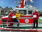 An Bord des Seenotrettungsbootes NEUHARLINGERSIELim Hafen von Neuharlingersiel stehen der freiwillige Vormann Heinz Steffens (l.) und der DGzRS-Ehrenamtliche Klaus Wilbers mit je einem symbolischen Spendenscheck in der Hand. Zwischen ihnen steht ju-com-Geschäftsführerin Monika Janßen, die diese überreicht hat.