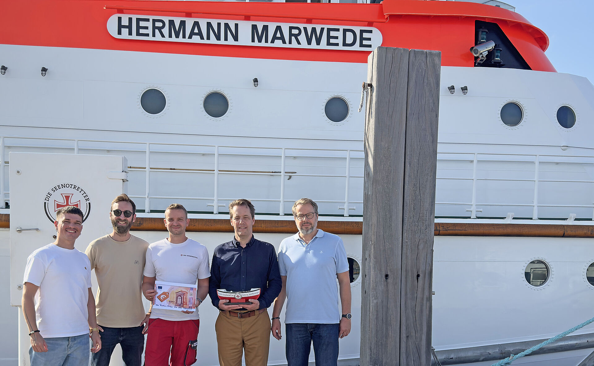 Spendenübergabe vor dem Seenotrettungskreuzer HERMANN MARWEDE: Zwei Mitarbeiter von „Fischers Fritze“ (v. l.) gemeinsam mit DGzRS-Vormann (m.) sowie zwei DGzRS-Mitarbeitern.