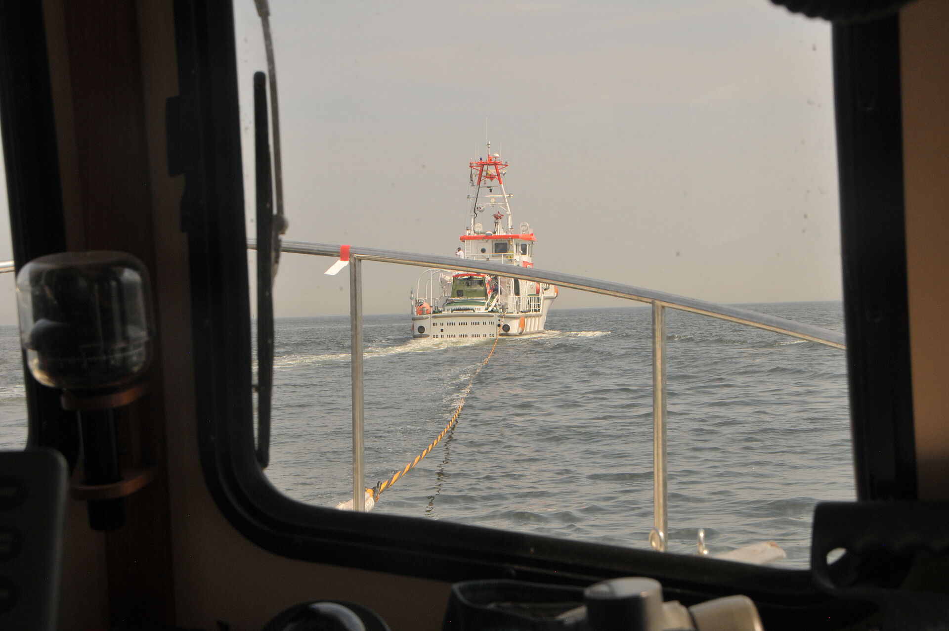 Aus dem Steuerstand eines Motorbootes ist der Seenotrettungskreuzer ANNELIESE KRAMER zu sehen. Eine Schleppleine verbindet die beiden Schiffe miteinander. 