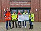 Vor dem DGzRS-Stationsgebäude in Cuxhaven, einem roten Klinkerbau, stehen die PKE-Ingenieure Marc Itgen (l.), Boris Garlt (2. v. l.), Lasse Schöttke (2. v. r.) und Nina Hagel (r.) Sie überreichen einen symbolischen Spendenscheck an DGzRS-Mitarbeiterin Sabine Preiß.