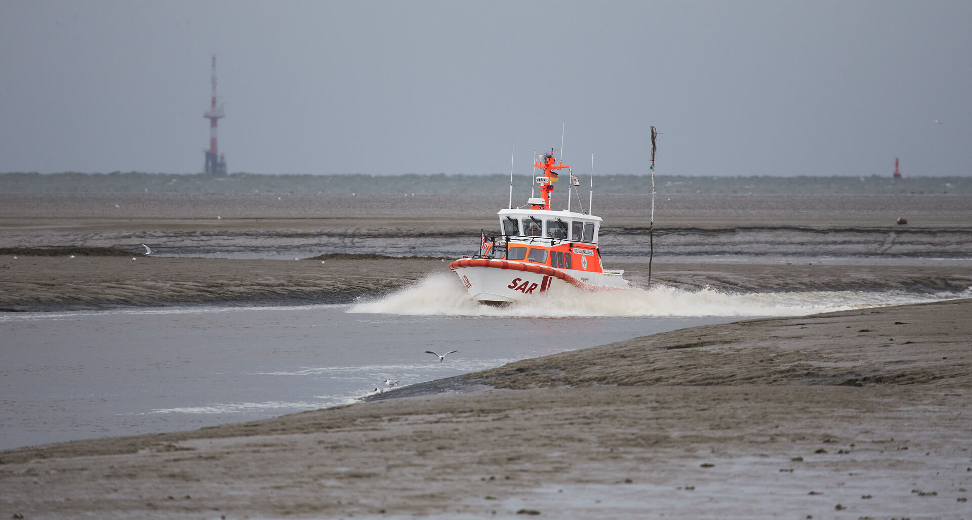 Ein Seenotrettungsboot fährt bei Niedrigwasser durch das enge Fahrwasser zwischen Wattgebieten.