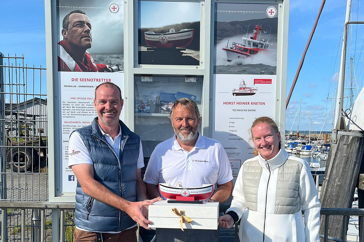 Spendenübergabe im Hafen vor Seenotretter-Schaukasten: Ehepaar übergibt dem freiwilligen Vormann Michael Petersen (r.) der DGzRS-Station Hörnum das Sammelschiffchen mit seiner Spende in Höhe von 1.000 Euro.