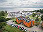 Im Vordergrund aus der Vogelperspektive ein Bild vom Hotel mit parkenden Autos davor, im Hintergrund sieht man den kleinen Yachthafen von Barhöft, mit vielen Segelbooten. Beides eingerahmt von Wald, der Himmel ist wolkenverhangen.