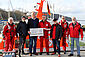 Vor einem Seenotrettungskreuzer steht der DGzRS-Geschäftsführer mit einem symbolischen Spendenscheck in der Hand sowie der Vormann der Freiwilligen-Station Langballigau mit einem Sammelschiffchen in der Hand inmitten dreier Besatzungsmitglieder der Station sowie zweier Mitglieder der Band „Santiano“.