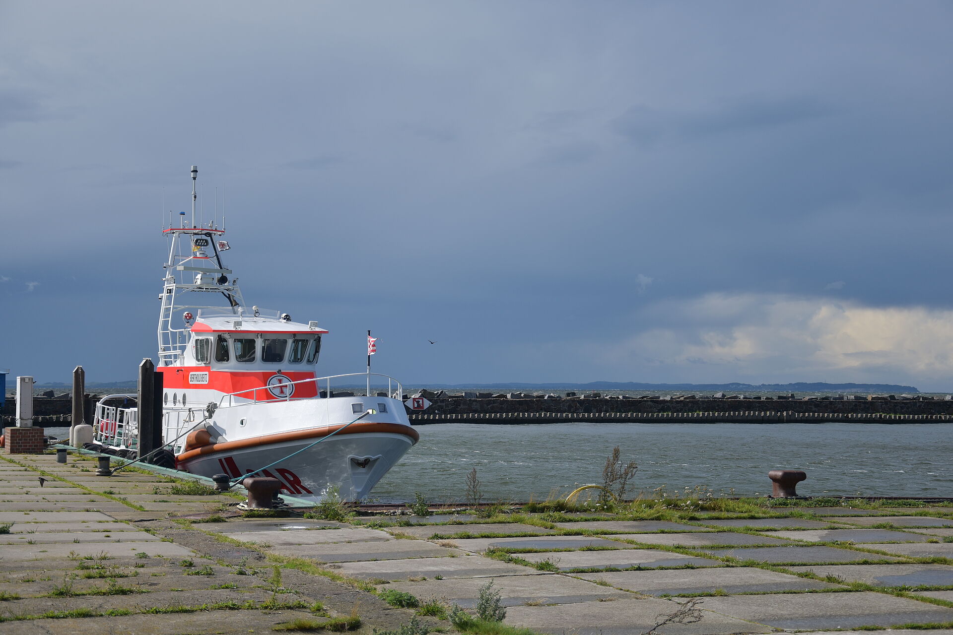 Der Seenotrettungskreuzer hat im einsamen Hafen festgemacht. Zugewachsene Betonplatten liegen im Hafen.